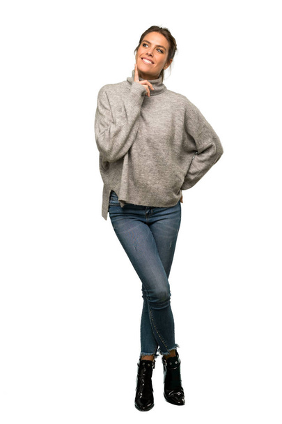 A full-length shot of a Blonde woman with turtleneck thinking an idea while looking up over isolated white background - Photo, Image