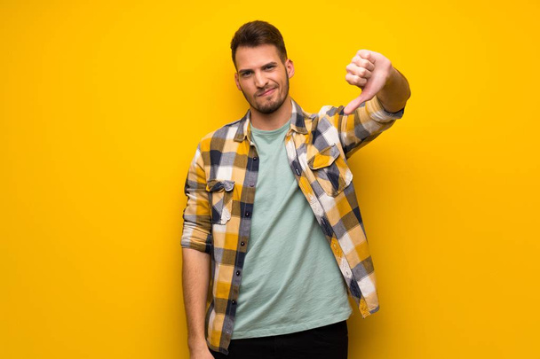 Handsome man over yellow wall showing thumb dowg with negative expression - Photo, Image