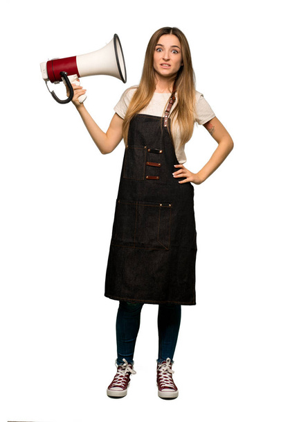 Full body Young woman with apron taking a megaphone that makes a lot of noise on isolated background - Foto, immagini