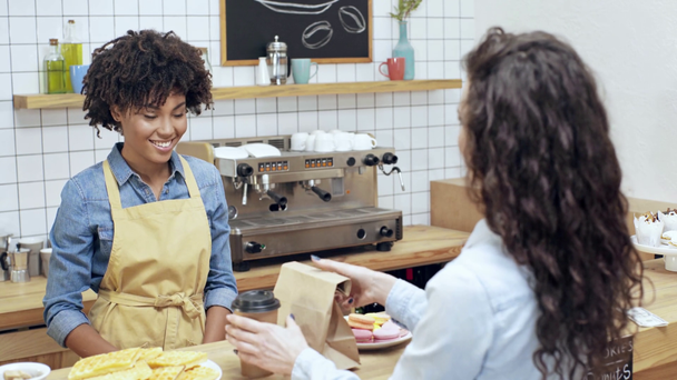 naispuolinen asiakas antaa rahaa hymyilevä afrikkalainen amerikkalainen naispuolinen kassanhoitaja ja poimien tilauksen kahvilassa
 - Materiaali, video