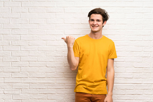 Чоловік-підліток над білою цегляною стіною, що вказує на бік, щоб представити продукт
 - Фото, зображення