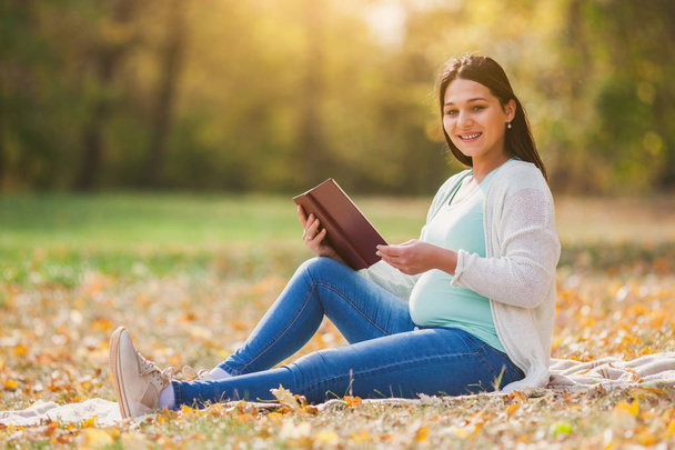 Terhes nő pihentető parkban. Ő is könyvet olvas. - Fotó, kép