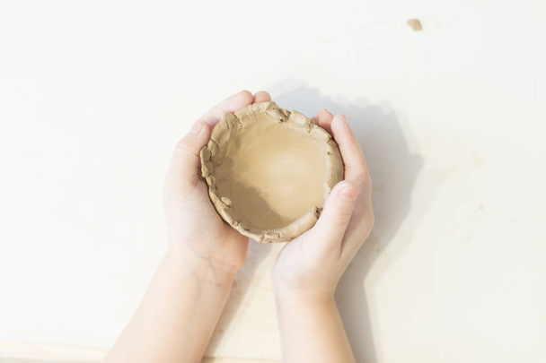 Children make clay. The hands of the child hold the clay. Light room. Clay dishes - Photo, Image