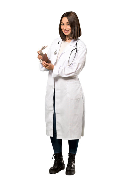 eine Ganzkörperaufnahme einer jungen Ärztin, die eine Brieftasche vor isoliertem weißen Hintergrund hält - Foto, Bild