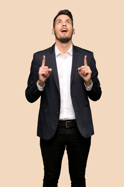 Handsome business man surprised and pointing up over ocher background - Fotoğraf, Görsel