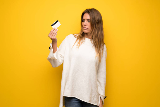Блондинка над жовтою стіною бере кредитну картку без грошей
 - Фото, зображення