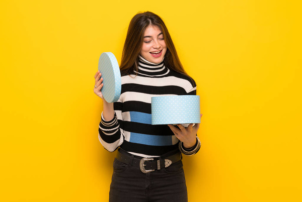 junge Frau über gelbe Wand mit Geschenkbox in der Hand - Foto, Bild