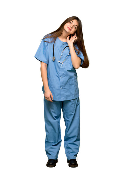 Full-length shot of Young nurse listening to something by putting hand on the ear on isolated white background - Valokuva, kuva