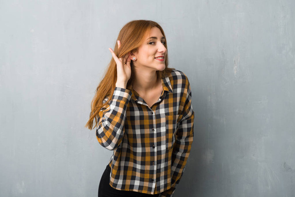 Jeune fille rousse sur le mur grunge écoute quelque chose en mettant la main sur l'oreille
 - Photo, image