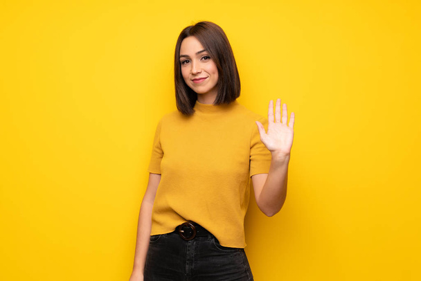 Jeune femme sur mur jaune saluant avec la main avec expression heureuse
 - Photo, image