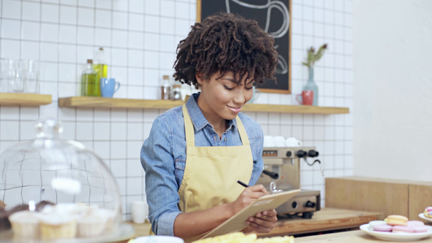 piękne african american kobieta Kasjer pisania w schowku za ladą w kawiarni - Materiał filmowy, wideo