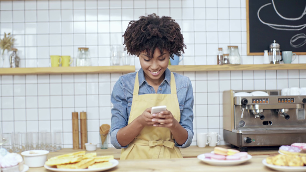 красивая африканская американка кассир показывает знак мира и утку лицо, делая селфи на смартфоне в кафе
 - Кадры, видео