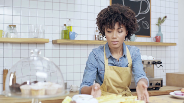 hermosa africana americana propietaria de café femenino en delantal de limpieza contador de postres con tela
 - Metraje, vídeo