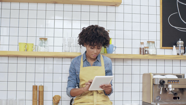 Cajero femenino afroamericano sentado en el mostrador y el uso de tableta digital en la cafetería
  - Metraje, vídeo