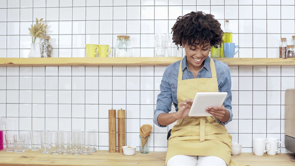 linda sorrindo africano americano caixa feminina sentado no balcão e usando tablet digital no café
  - Filmagem, Vídeo
