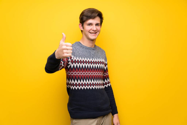 Teenager man over yellow wall with thumbs up because something good has happened - Foto, Imagem