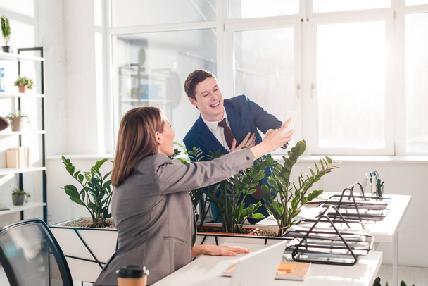 businesswoman holding smartphone and laughing with coworker in office  - Foto, Bild