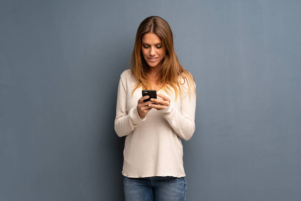 Mulher loira sobre fundo cinza enviando uma mensagem com o celular
 - Foto, Imagem