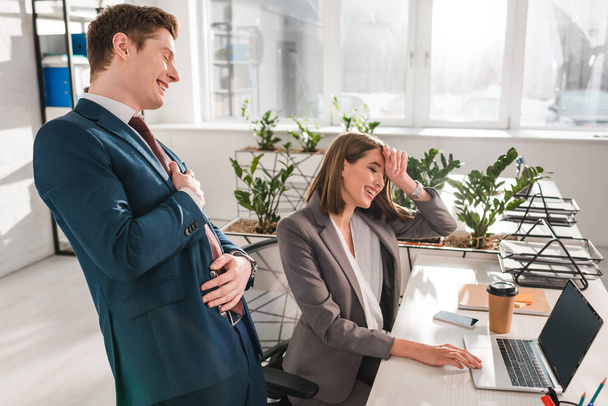 cheerful businesswoman laughing with coworker near laptop in office  - Foto, Bild