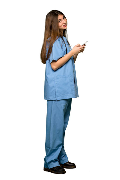 Full-length shot of Young nurse sending a message with the mobile on isolated white background - Фото, изображение