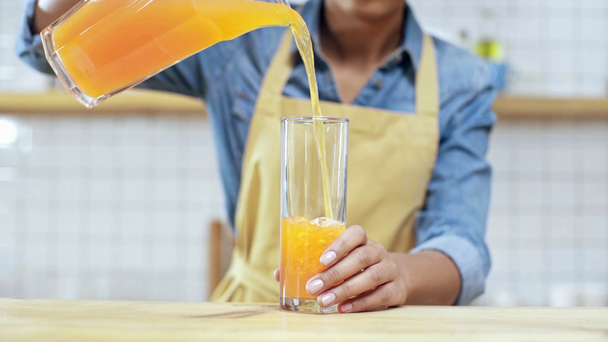 vista cortada de Africano americano fêmea dono de café em avental colocando vidro no balcão e derramando suco de laranja
 - Filmagem, Vídeo