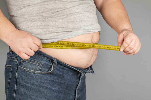 Чоловік вимірює жирний живіт за допомогою мірної стрічки. на сірому фоні
 - Фото, зображення