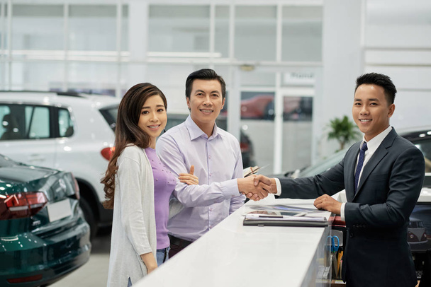 Cheerful Asian couple and salesman completing documents after buying new car - Photo, Image