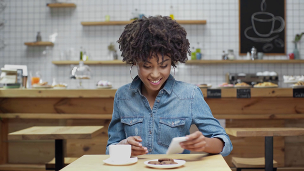číšnice přiblížit krásné usměvavé afroamerické zákaznici v kavárně kávu a soubory cookie - Záběry, video