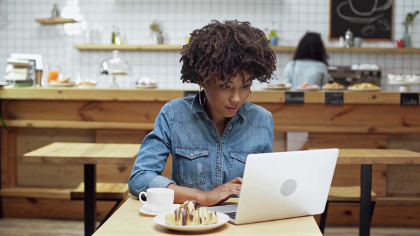 красивая африканская американка-фрилансер сидит за столом, пьет кофе и пользуется ноутбуком в кафе
 - Кадры, видео
