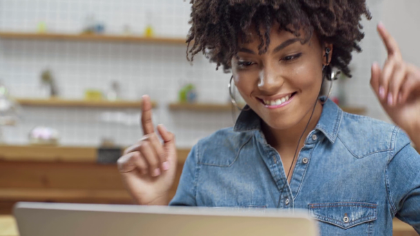 bela mulher americana africana sorridente em fones de ouvido usando laptop e ouvir música no café com espaço de cópia
 - Filmagem, Vídeo
