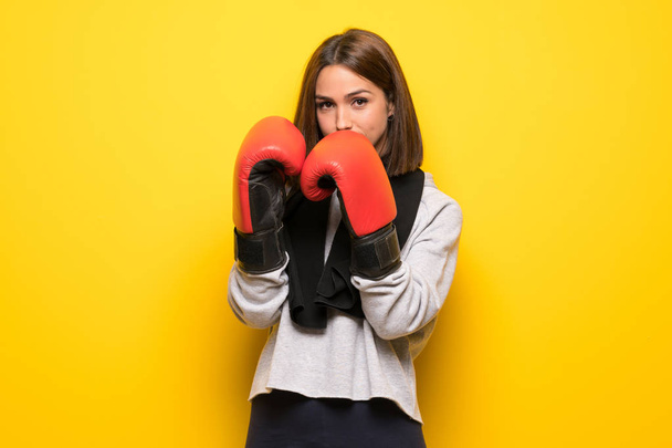 ボクシング グローブと黄色の背景の上の若いスポーツ女性 - 写真・画像