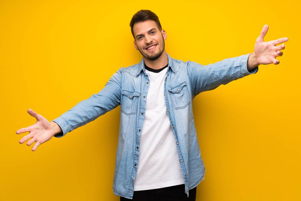 Handsome man over yellow wall presenting and inviting to come with hand - Fotoğraf, Görsel