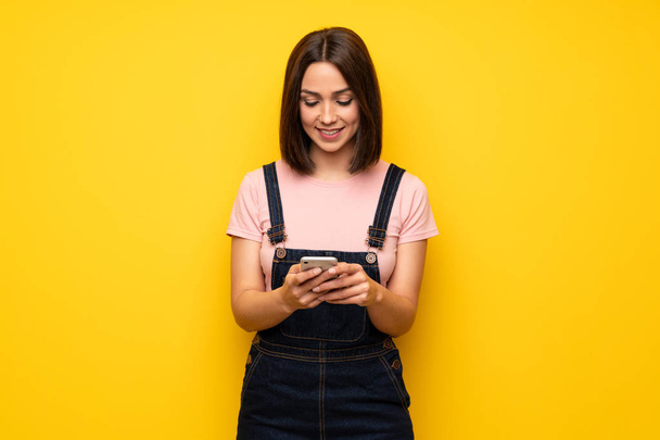 Giovane donna sopra il muro giallo che invia un messaggio con il cellulare
 - Foto, immagini