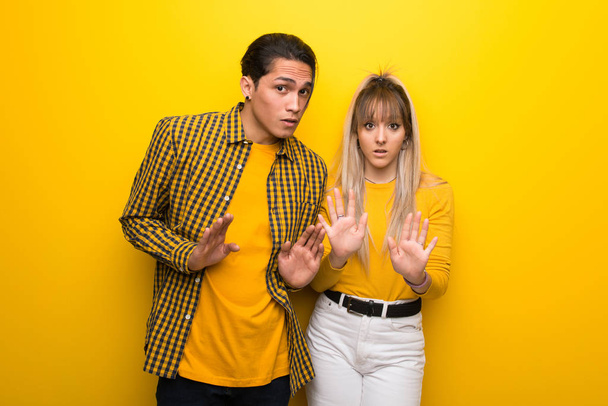 Young couple over vibrant yellow background making stop gesture with both hands - Zdjęcie, obraz
