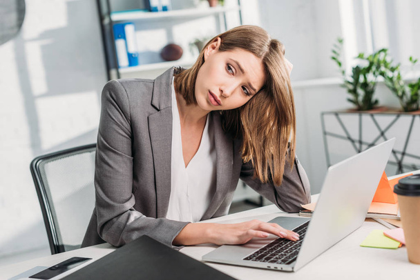 tired attractive businesswoman sitting near laptop in office  - Photo, Image