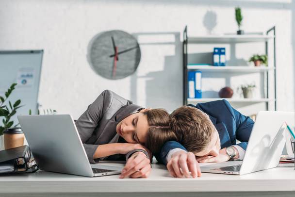 colleghi stanchi che dormono alla scrivania vicino ai computer portatili in ufficio
  - Foto, immagini