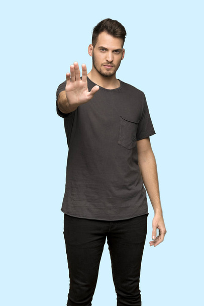 Man with black shirt making stop gesture denying a situation that thinks wrong over blue background - Foto, Imagen