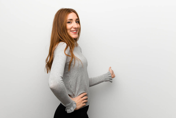 Redhead girl over white wall pointing back and presenting a product - Фото, зображення