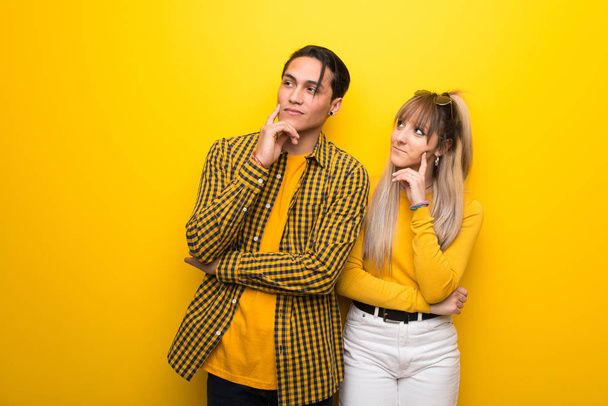 Young couple over vibrant yellow background thinking an idea while looking up - Photo, image