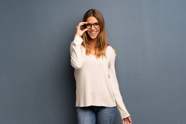 blonde Frau über grauem Hintergrund mit Brille und lächelnd - Foto, Bild