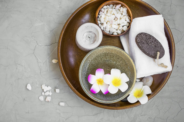 Spa products in wooden tray, top view of spa items with frangipani flowers, candle, bath salt, towel and ponce stone, spa still life setting - Фото, зображення