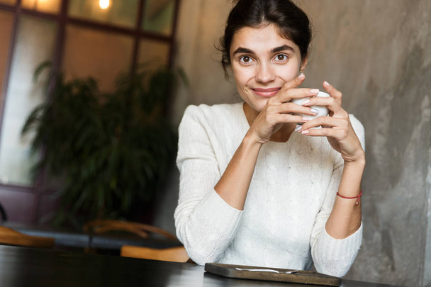 Image of beautiful young woman sitting in cafe drinking coffee indoors. - Zdjęcie, obraz