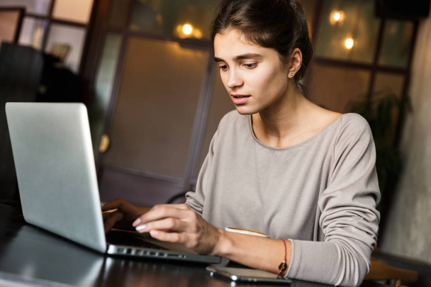 Kapalı dizüstü bilgisayar kullanan kafede oturan genç ve güzel kadın fotoğrafı. - Fotoğraf, Görsel
