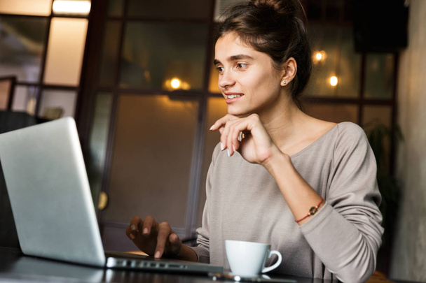 Foto de una mujer bastante joven sentada en un café en el interior usando una computadora portátil
. - Foto, imagen
