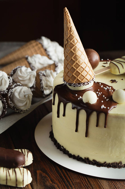 Белый шоколадный торт, украшенный мороженым на палочке, вафельной шишкой и шоколадными шариками. Детский праздничный торт. детский торт
 - Фото, изображение