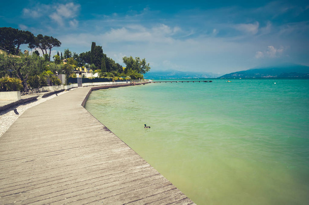 a long pier along the shore of beautiful lake Garda, Italy - 写真・画像