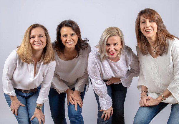 Группа из 4 женщин, друзей, среднего возраста, развлекающихся на фотосессии в студии с белым фоном
 - Фото, изображение