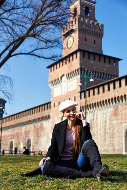 Milan, Italie - 18 février 2019 Pose de mannequin avec un poire rouge, une écharpe et un manteau noir pour un portrait avec Castelo Sforzesco à Milan en arrière-plan par une journée ensoleillée
 - Photo, image