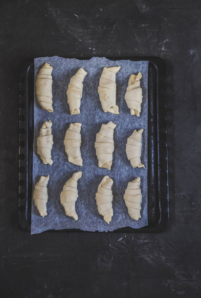 Raw croissants with chocolate on a baking sheet before baking. Top view on dark background and white parchment. Fly lay - Фото, зображення