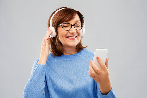 senior woman in headphones listening music on cell - Fotografie, Obrázek